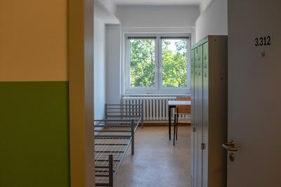 Blick in einen Raum der Gemeinschaftsunterkunft Luisenhof. Zwei Bettgestelle, Schränke und ein Tisch mit zwei Stühlen stehen in dem kleinen Zimmer an der Wand.